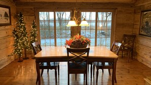 A wooden cabin interior with a dining table, chairs, a Christmas tree, and a large window. - Log Inn on Madison Lake.   Multi generation. Corporate retreat for team building (Madison lake)