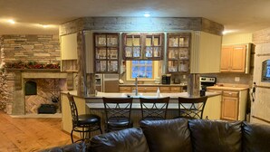 A cozy kitchen with a stone fireplace, wooden cabinets, and a bar area with stools. - Log Inn on Madison Lake.   Multi generation. Corporate retreat for team building (Madison lake)