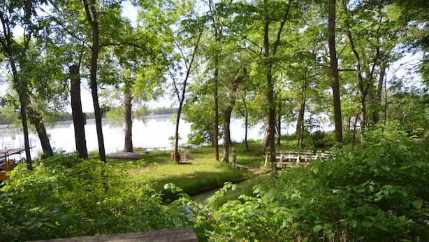 A serene lakeside setting with a wooden deck, picnic table, and lush greenery. - Log Inn on Madison Lake.   Multi generation. Corporate retreat for team building (Madison lake)