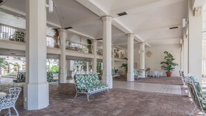 A spacious indoor area with brick flooring, white columns, and multiple seating arrangements including a patterned sofa and white chairs. - PALM BEACH HOTEL CONDO DESIGNER CHIC ONE BEDROOM (Palm Beach)