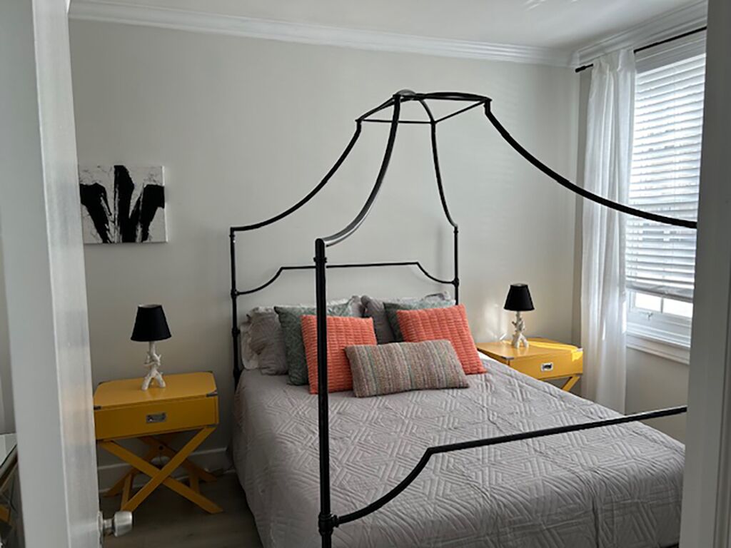 A bedroom with a four-poster bed, two bedside tables, and a window with blinds.