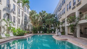 A swimming pool surrounded by palm trees and lounge chairs, with multi-story buildings in the background. - PALM BEACH HOTEL CONDO DESIGNER CHIC ONE BEDROOM (Palm Beach)