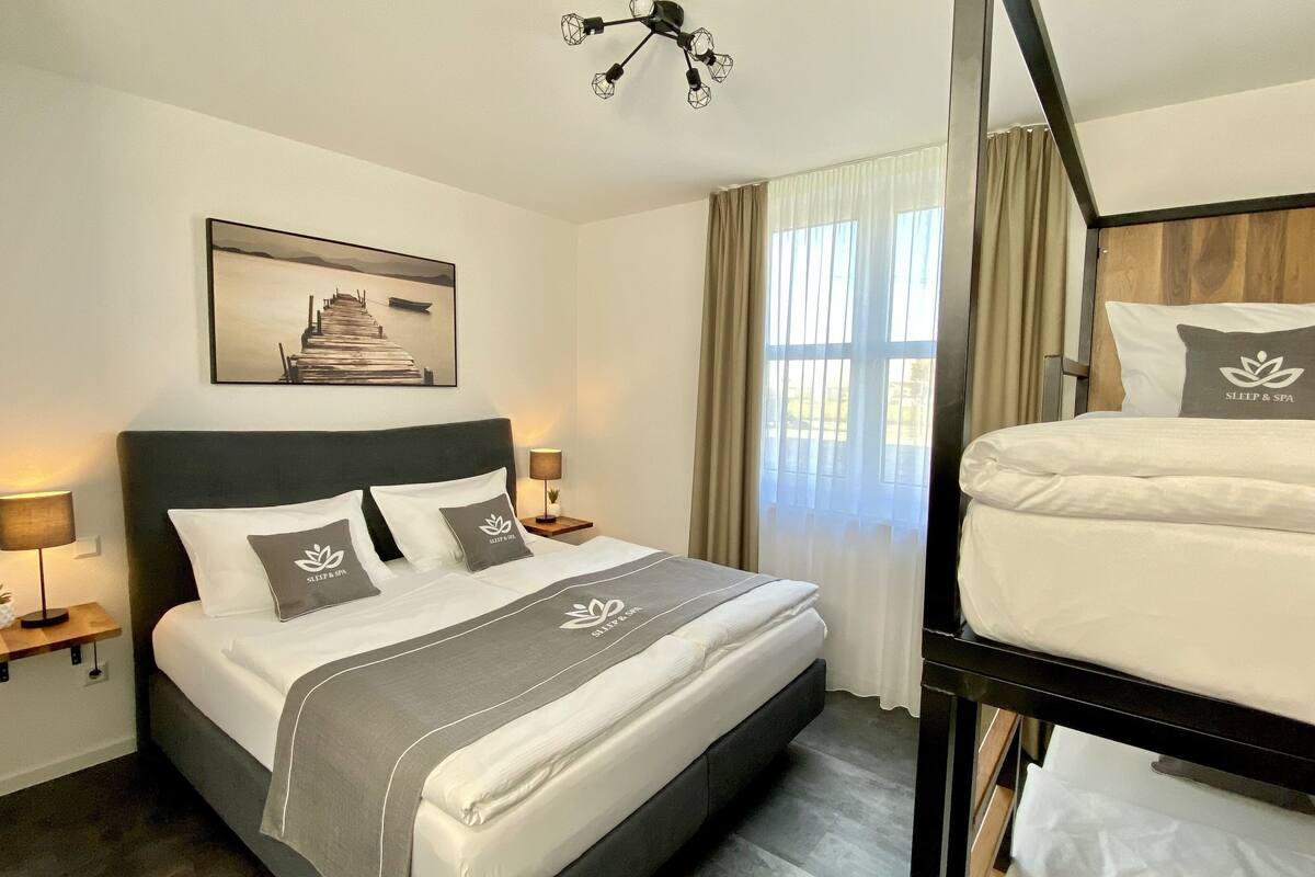 Une chambre d’hôtel comprenant un lit, un deuxième lit, une table de chevet avec une lampe, un tableau accroché au mur et un luminaire au plafond.