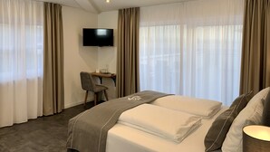 Una habitación de hotel con cama, escritorio, silla, televisor y cortinas.