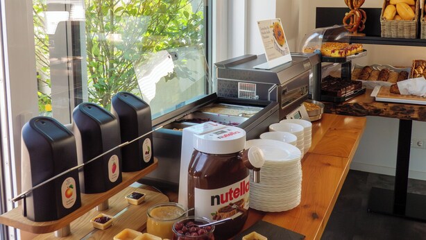 Un bufé de desayuno con diversas opciones de alimentos, una máquina de café y una ventana con vistas a zonas verdes.