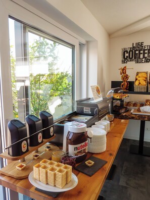 Un bufé de desayuno con diversas opciones de alimentos, una máquina de café y una ventana con vistas a zonas verdes.