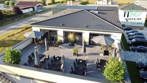 Un hotel con techo de tejas, zona de estar al aire libre con sombrillas y aparcamiento.