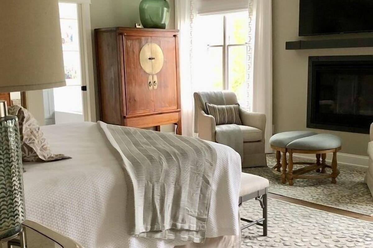 A bedroom with a bed, a wooden cabinet, a chair, a bench, and a television mounted on the wall.
