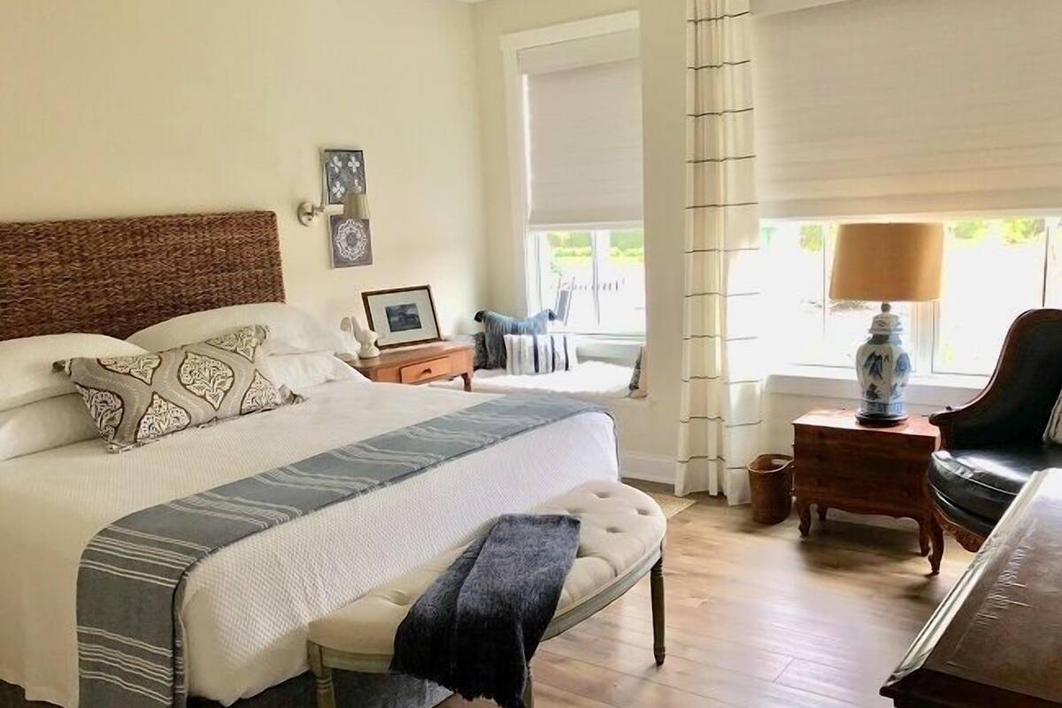 A neatly arranged bedroom with a bed, bedside table, lamp, chair, and window.