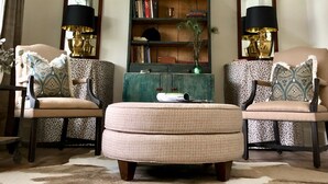 A cozy living room with a round coffee table, two armchairs, a bookshelf, and a large mirror. - The Farmhouse (Hammonton)