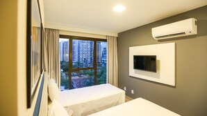 Habitación de hotel con cama, televisor en la pared y ventana con cortinas.