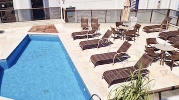 A rooftop pool area with a rectangular pool, lounge chairs, and a table with an umbrella.