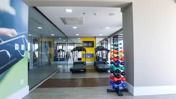 Un gimnasio con cintas de correr, máquinas de pesas y una pared llena de mancuernas de colores.