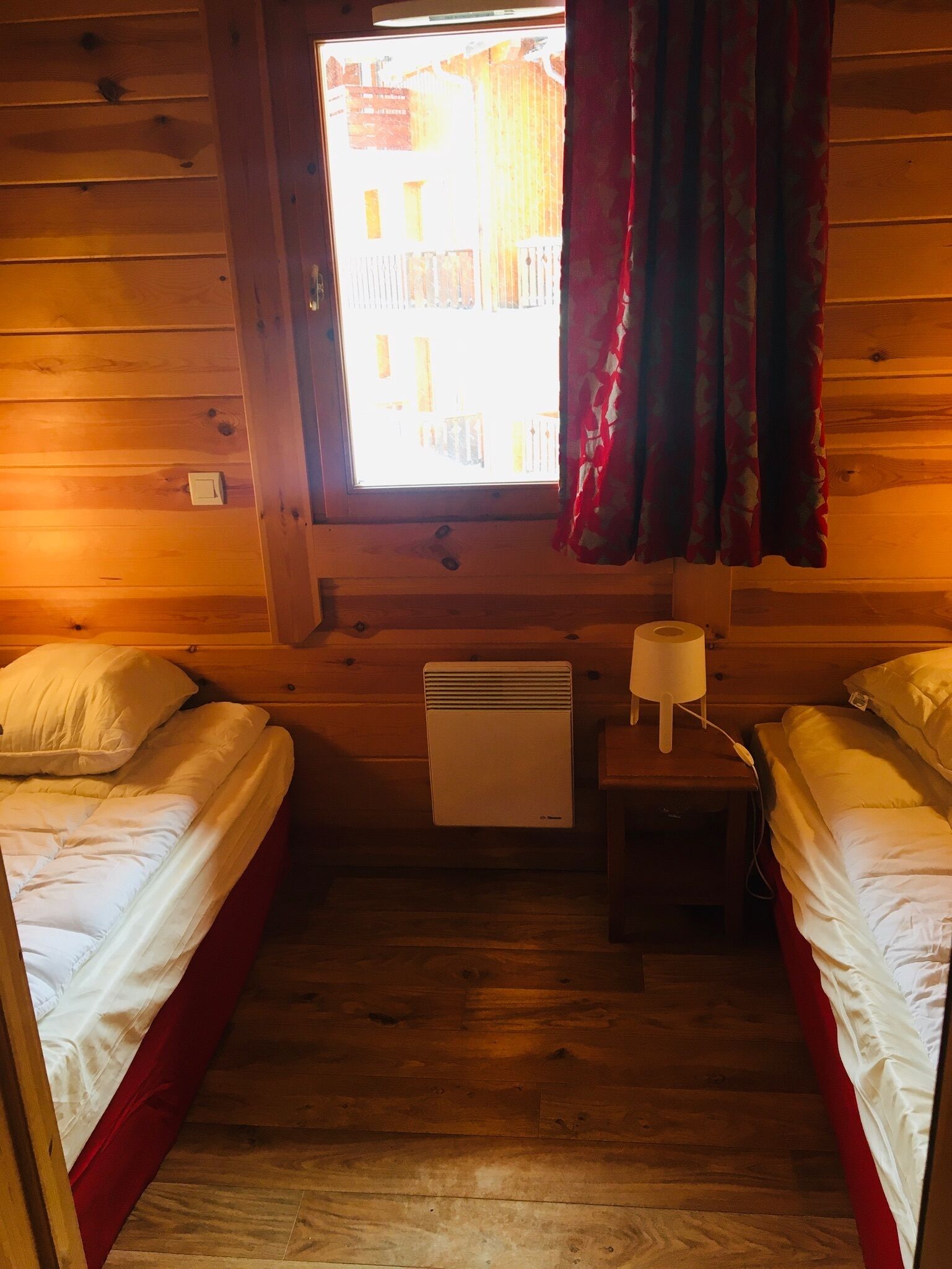A small, cozy room with two beds, a heater, a lamp, and a window with curtains.