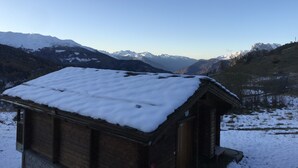 Une cabane en bois, dont le toit est recouvert de neige, nichée au cœur d’un paysage montagneux.