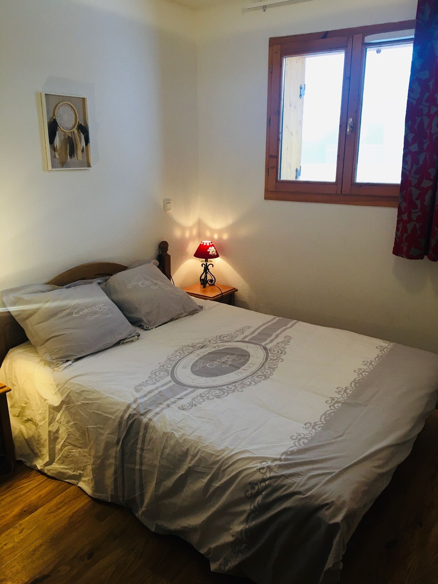 Un dormitorio con cama, mesita de noche, lámpara, ventana con cortinas y decoración en la pared.