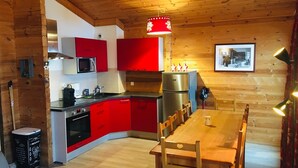 Une cuisine compacte avec des meubles rouges, un réfrigérateur en acier inoxydable et un coin repas avec des chaises en bois.