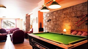 Une salle de billard équipée d’une table de billard, de sièges confortables, de murs en pierre et d’un éclairage d’ambiance.