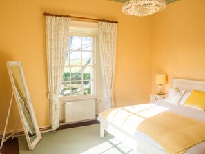 A bedroom with a bed, a nightstand, a lamp, a window with curtains, and a radiator. - Kill House (Clifden)
