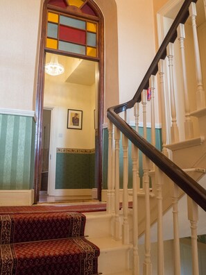 Un escalier avec des balustrades blanches et une main courante sombre, menant à une porte ornée d’un vitrail.