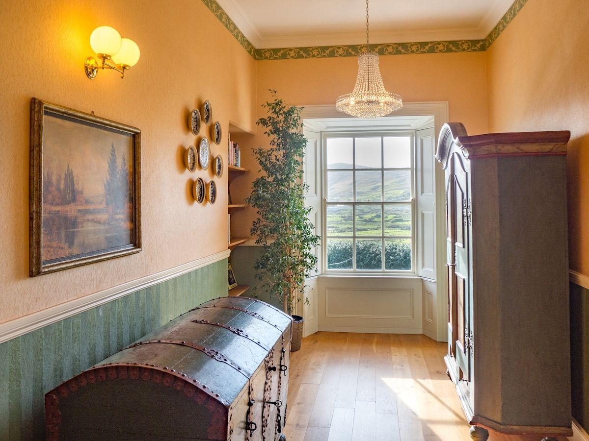 Quarto com um banco de madeira, um candelabro, uma janela grande e uma porta.