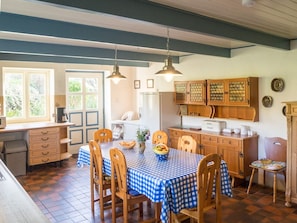 A dining area with a checkered tablecloth, wooden chairs, and a kitchen in the background.