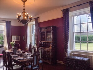 Une salle à manger avec une table dressée pour quatre personnes, un lustre et une grande fenêtre donnant sur l’extérieur.