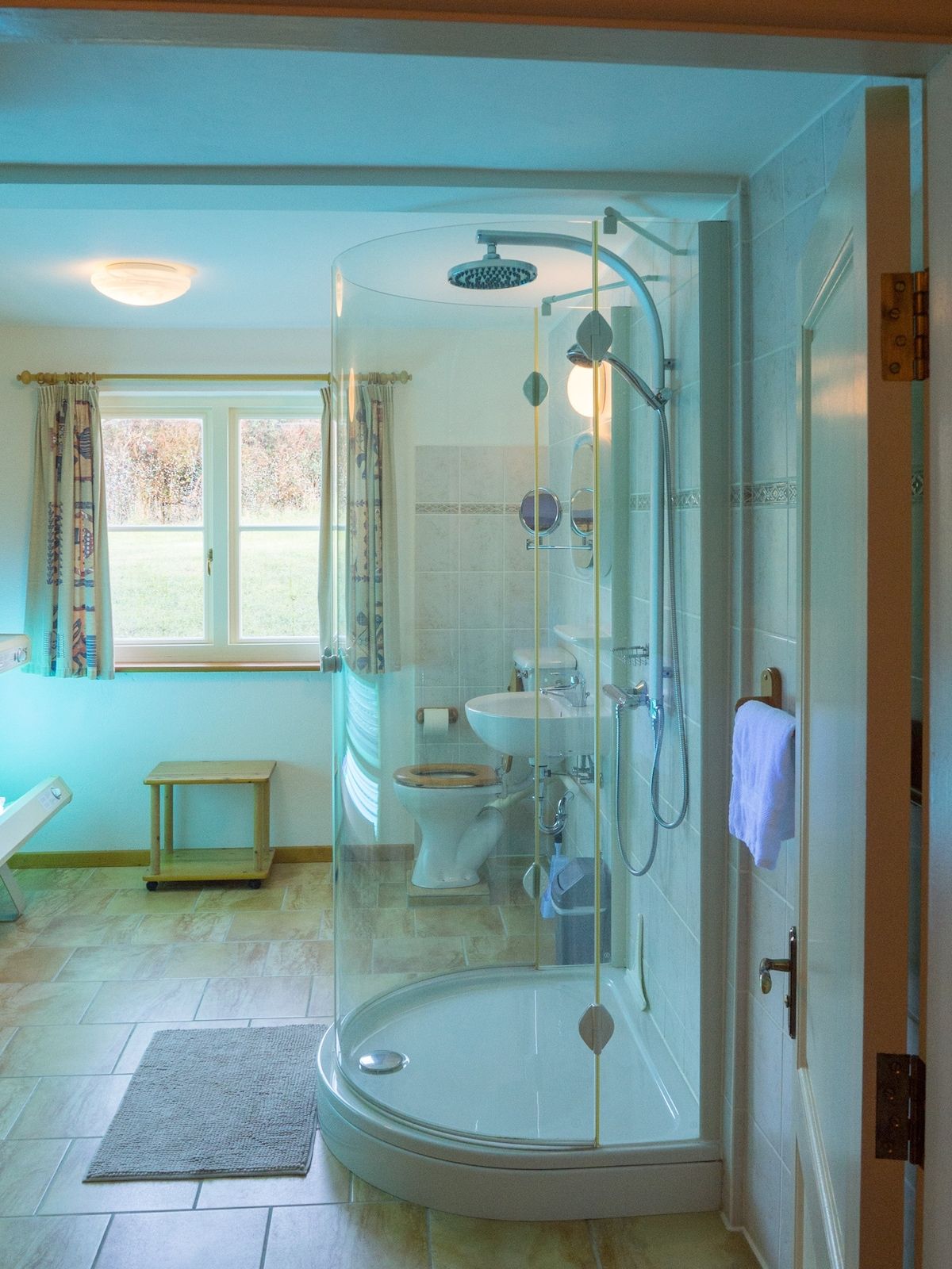 A bathroom with a glass-enclosed shower, a toilet, a sink, and a small wooden bench.