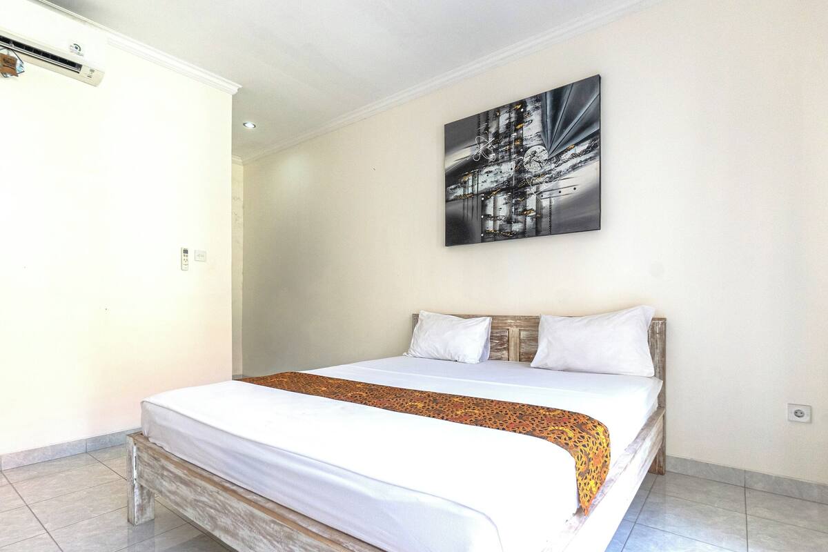 A hotel room with a bed, a headboard, a wall-mounted artwork, and a visible air conditioning unit.