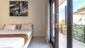A bedroom with a bed, a painting, and a balcony with a view of greenery. - Azalea Homestay & Villa (Canggu)