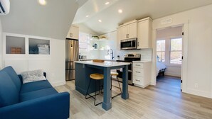 Una cocina moderna con electrodomésticos integrados, un comedor con sofá azul y vistas al exterior.