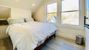 Un dormitorio con una cama, dos ventanas, una lámpara en el techo y un cubo de basura.