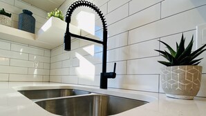 Una cocina con un lavamanos de acero inoxidable, salpicadero de azulejos blancos y una planta en maceta sobre la encimera.
