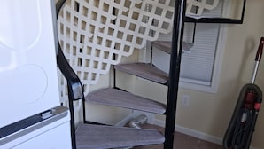 A spiral staircase with a white lattice design, a vacuum cleaner, and a window with blinds.