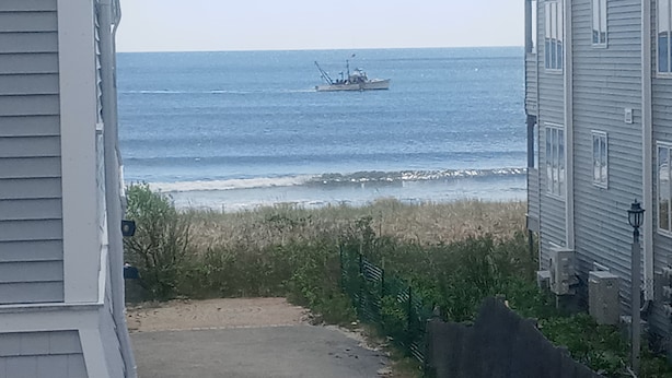 A coastal view with a pathway leading to the beach, a boat in the water, and a house with a visible porch.