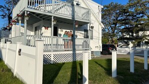 A two-story white house with a balcony, a picket fence, and a lawn.