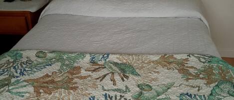 A bed with a white quilt, two pillows with a blue and white pattern, and a coral reef design on the bedspread.