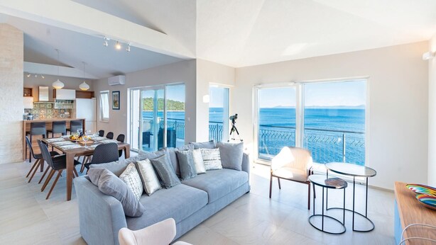 A spacious living area with a grey sofa, dining table, and chairs. A balcony with a view of the sea is visible. - Awesome home in Smokvica (Smokvica)