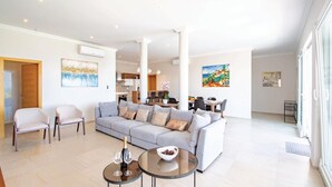 A spacious living room with a grey sofa, two armchairs, and a coffee table with a bottle and glasses. There is a dining area in the background with a table and chairs. - Awesome home in Smokvica (Smokvica)