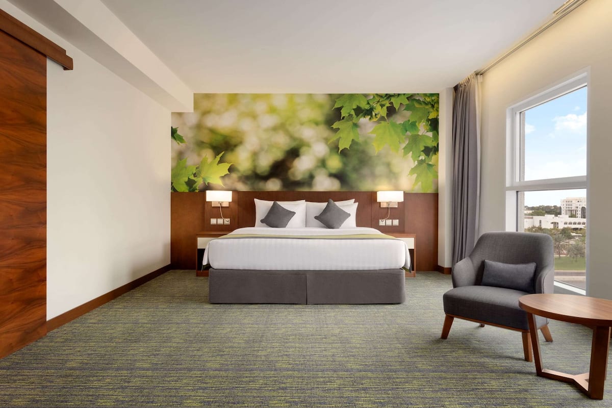 A hotel room with a bed, a chair, a small table, and a large window.