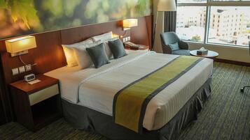 A hotel room with a large bed, two bedside tables, a chair, a small table, and a window with a city view.