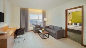 A hotel room with a desk, two armchairs, a sofa, a coffee table, and a bed.