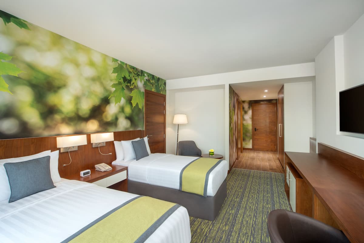 A hotel room with two beds, a desk, a TV, and a large wall mural.
