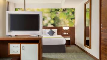 Una habitación de hotel con una cama, un escritorio con televisor, una mesita de noche y un espejo.