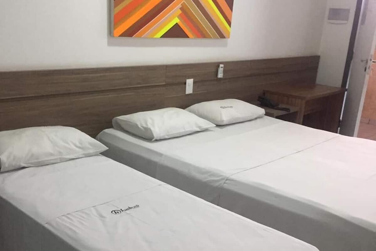 A hotel room with two single beds, a wooden headboard, a small bedside table with a lamp, and a colorful abstract painting on the wall.