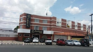 A multi-story building with a prominent 'Jambura Hotel' sign. There are several parked cars in front, and the building has a brick facade with white trim. - Samburá Hotel - Feira de Santana (Feira de Santana)