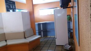 A small kitchenette with a refrigerator, a sink, and a countertop. There is a sofa in the corner and a window providing natural light. - Samburá Hotel - Feira de Santana (Feira de Santana)