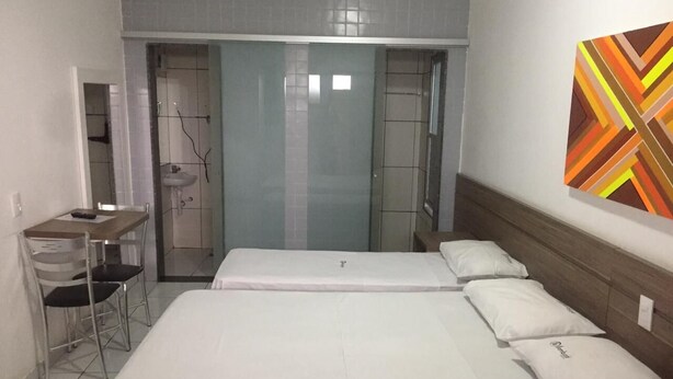 A hotel room with a bed, a desk, and a chair. There is a bathroom with a shower and a sink. - Samburá Hotel - Feira de Santana (Feira de Santana)