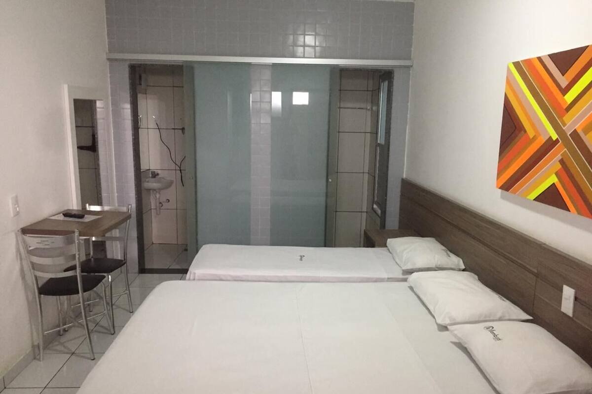 A hotel room with a bed, a desk, and a chair. There is a bathroom with a shower and a sink.