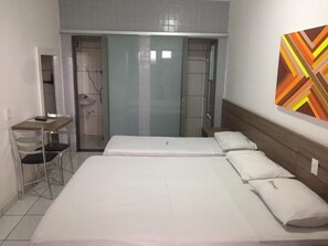 Quarto de hotel com cama, escrivaninha e cadeira. Inclui banheiro com chuveiro e pia.